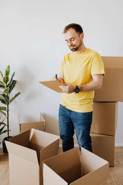 A man and a woman engaged in a home relocation process inside a moving van, surrounded by stacked brown cardboard boxes of varying sizes, some open and others sealed with packing tape, all neatly arra