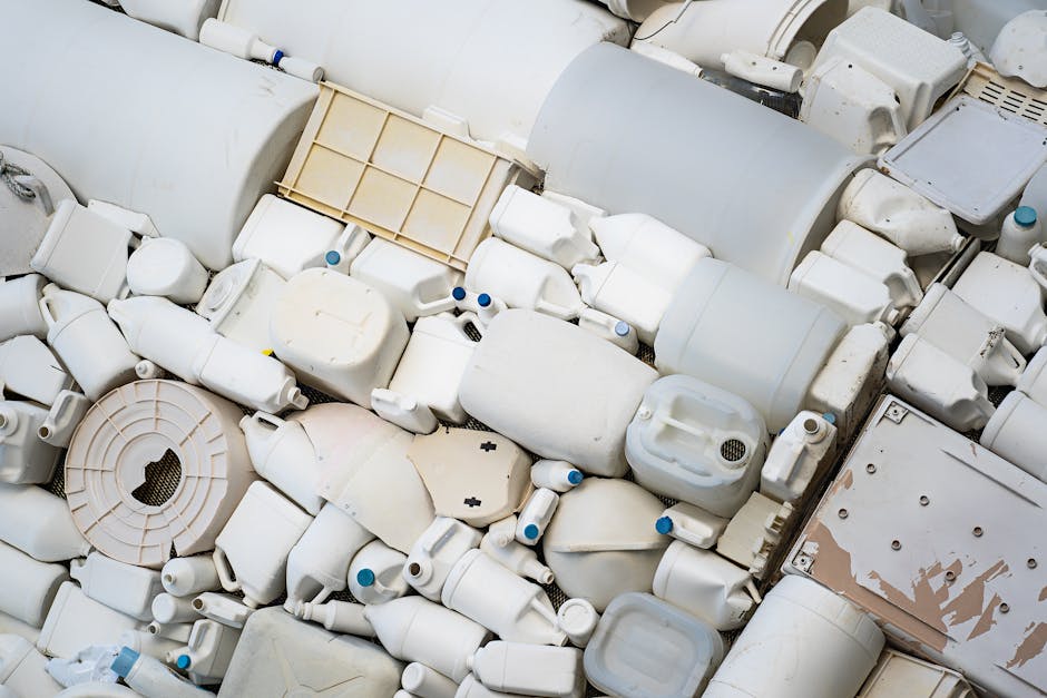 A large pile of discarded white plastic bottles, containers, and bathroom fittings, including sinks, toilet parts, and various pipe sections, situated outdoors on a pavement next to a property entrance. The items are haphazardly stacked, with some plastic wrap and foam packaging materials visible among them. A moving van is partially visible in the background, along with a doorway leading into a building. The scene depicts a home relocation removal process involving waste disposal and the sorting of reusable or recyclable items, consistent with the services offered by Man with Van Tottenham in the context of house removals and furniture transport within Tottenham.